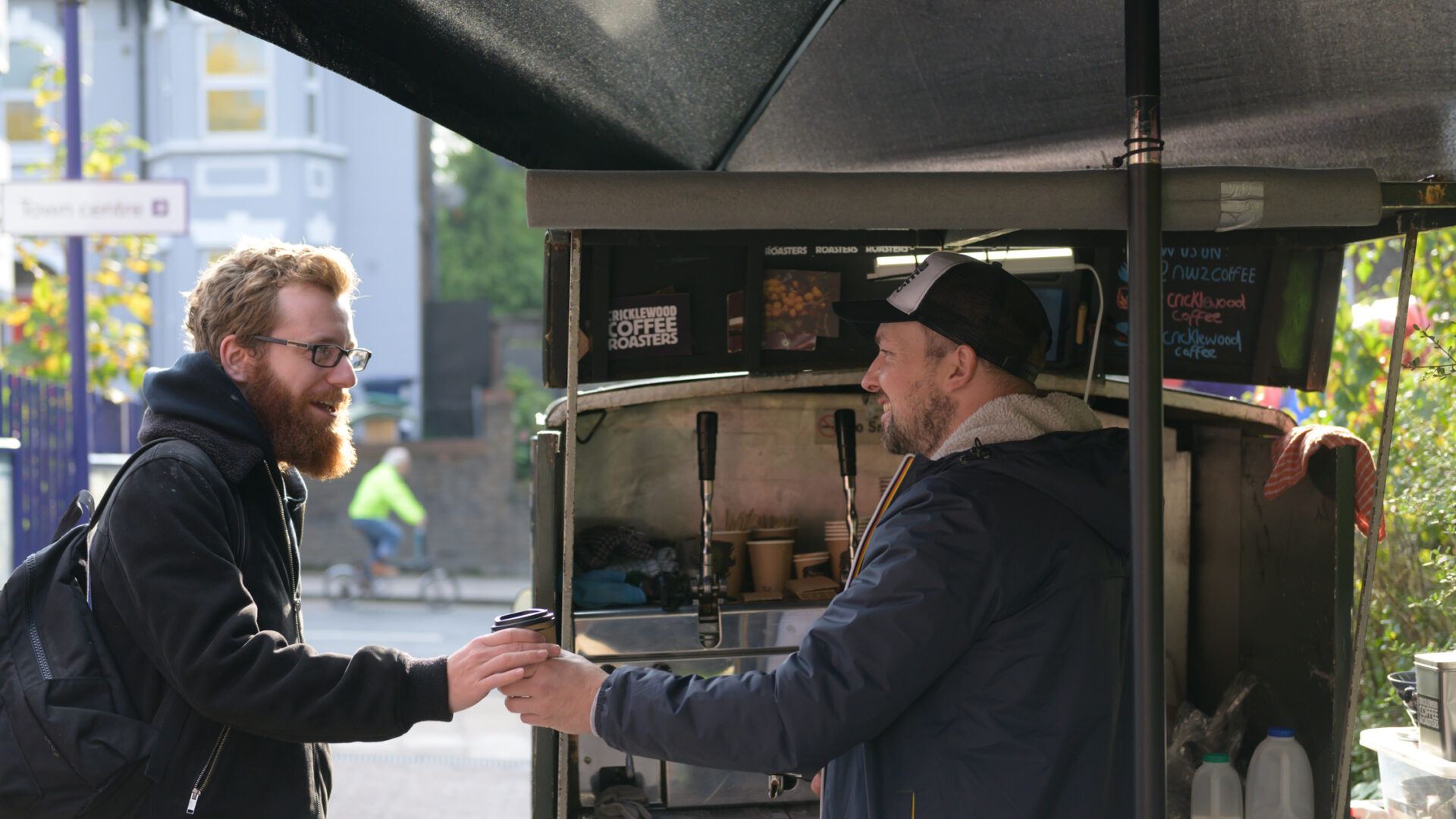 Man handing customer a cup of coffee outside cart (Brent Cross Town)