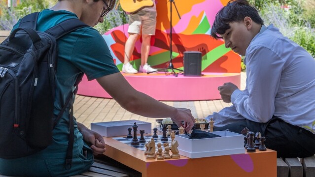 Photo of people playing chess in Neighbourhood Square in Brent Cross Town, while someone performs live music in the background. (Brent Cross Town)